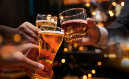 Three hands are holding different alcoholic drinks in a cheers gesture.